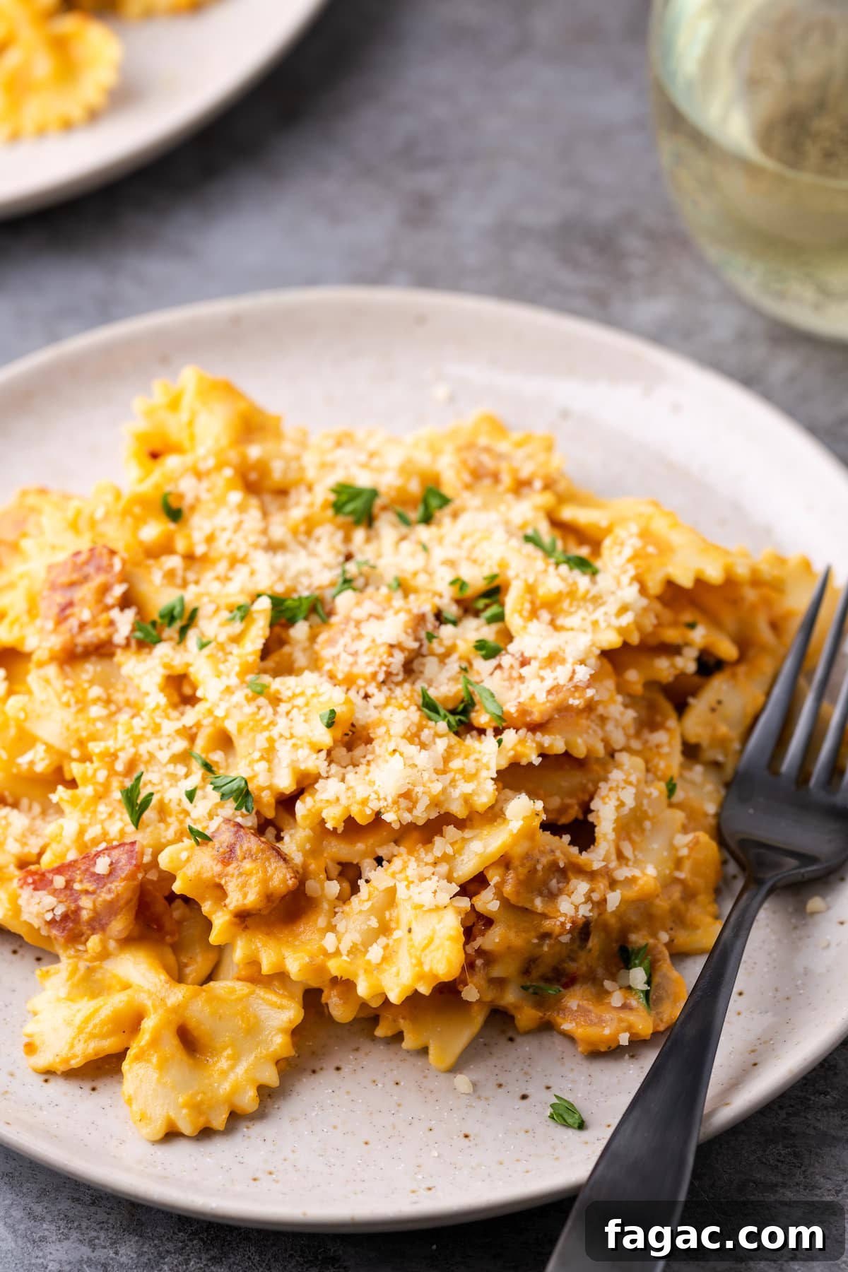 A serving of pumpkin pasta with bacon on a plate next to a fork.