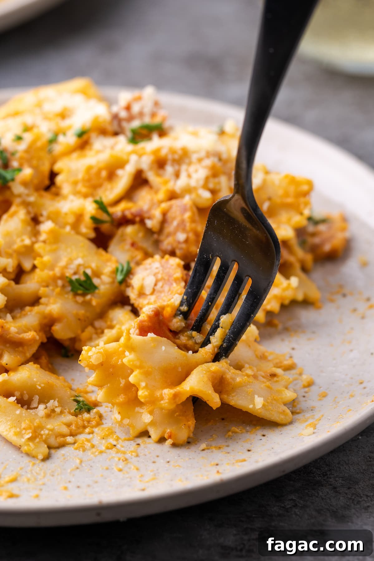 A fork picks up a bite of farfalle pumpkin pasta with bacon from a plate.