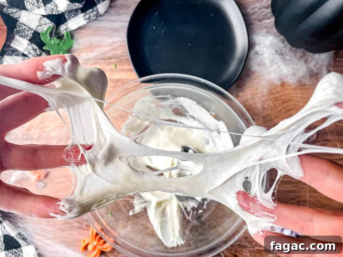 Fingers spread apart with melted marshmallows spread between the fingers, making a spider web