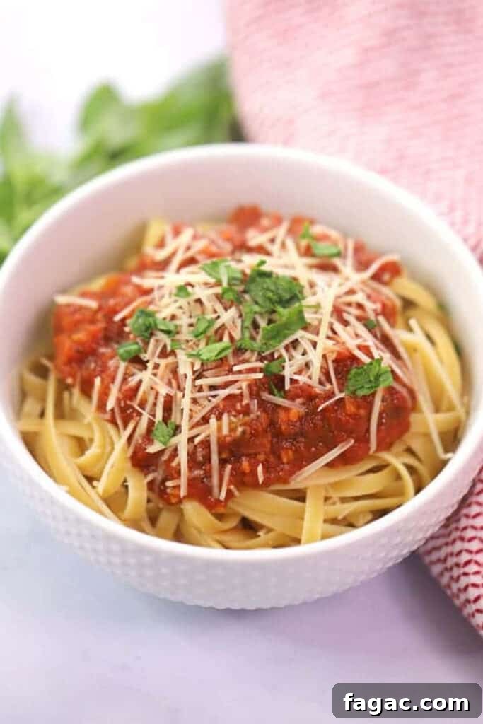 A white bowl full of fettuccini noodles topped with marinara sauce, Parmesan cheese and fresh basil. 