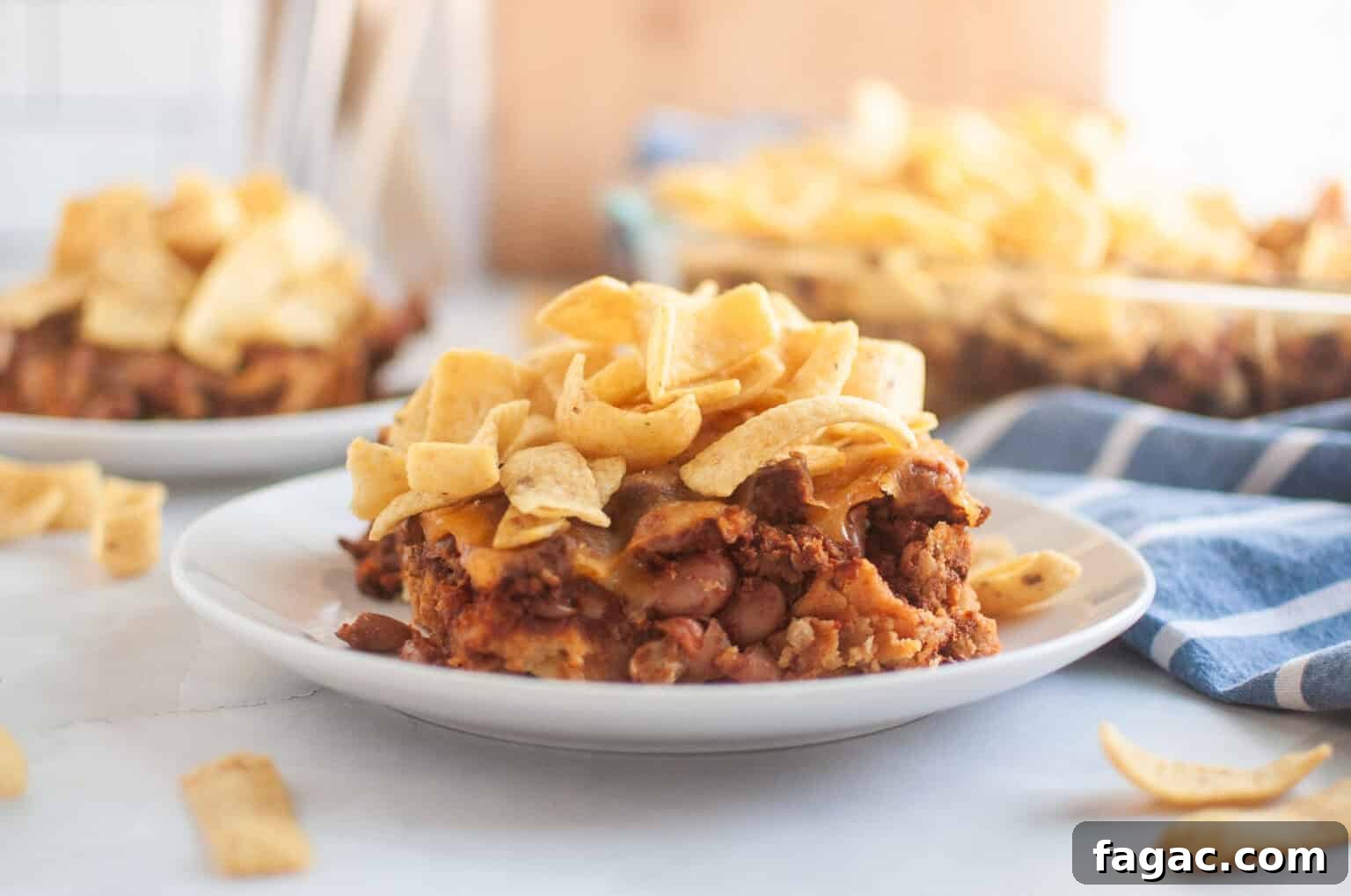 23 Classic Casseroles That Taste Like Grandma’s Comfort Cooking 2 A white plate with a serving of Frito pie, topped with corn chips, is shown on a light surface.