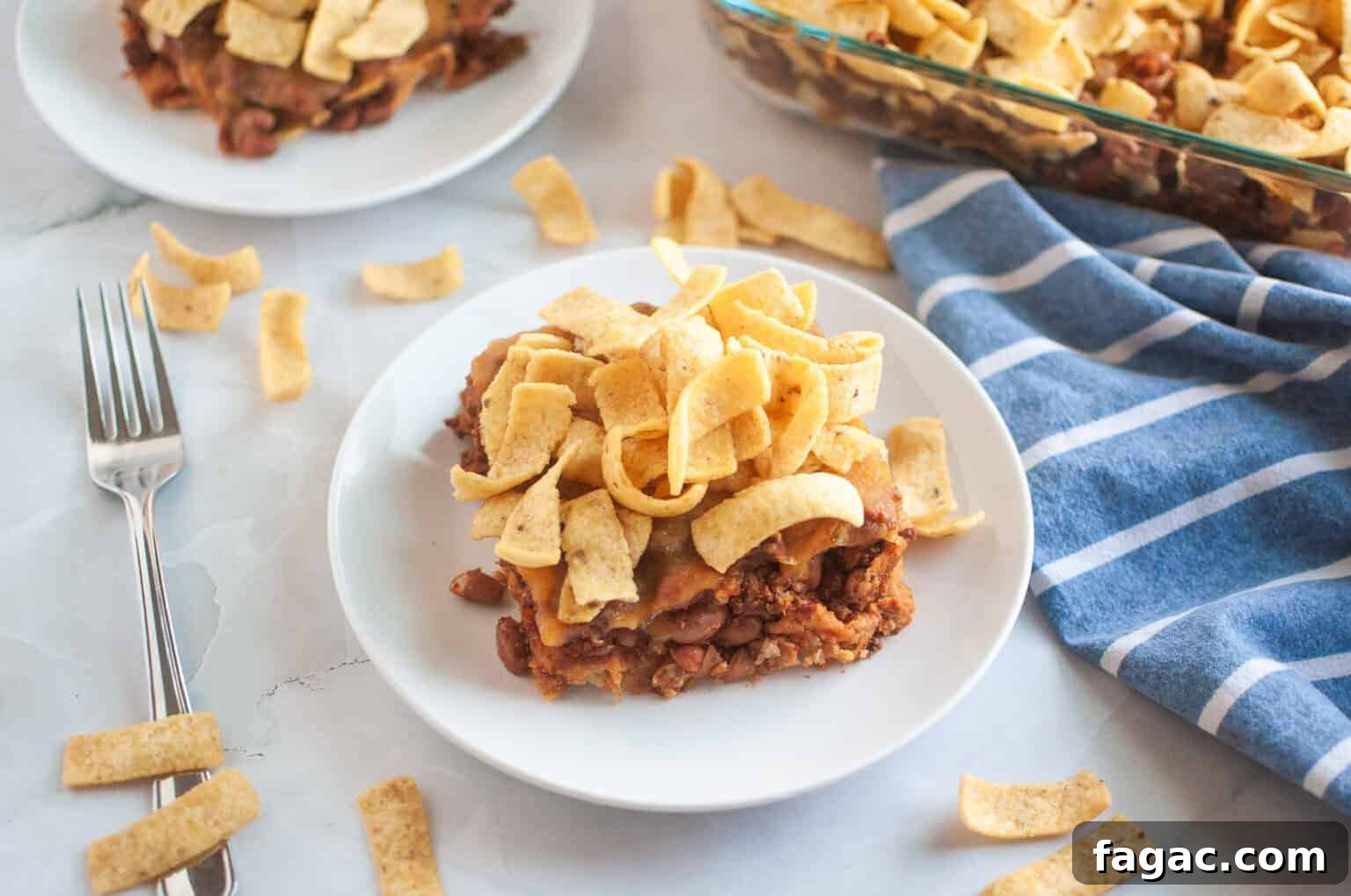 23 Classic Casseroles That Taste Like Grandma’s Comfort Cooking 16 A white plate with a serving of Frito pie, topped with corn chips, is shown on a light surface.