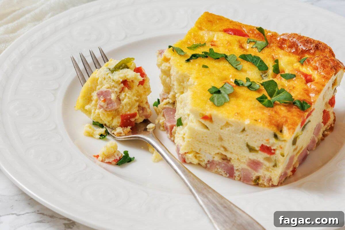 23 Classic Casseroles That Taste Like Grandma’s Comfort Cooking 7 A slice of baked Western omelet with ham, red peppers, and herbs is served on a white plate with a fork holding a bite-sized piece.