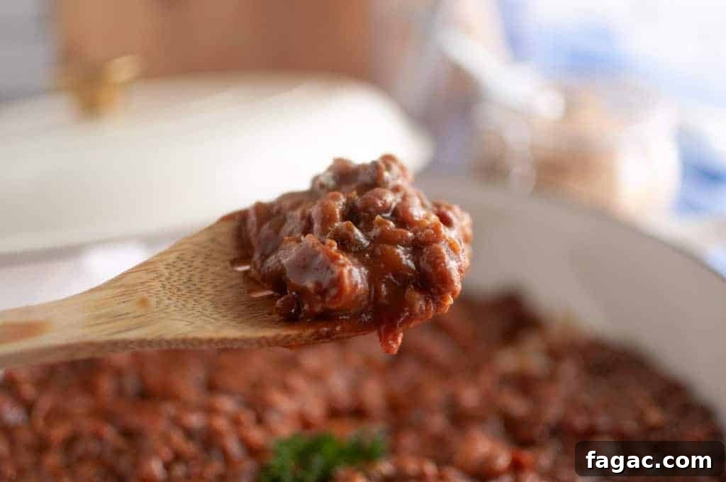 23 Classic Casseroles That Taste Like Grandma’s Comfort Cooking 9 A close-up of a wooden spoon holding a serving of baked beans casserole, with a pot of chili in the background.