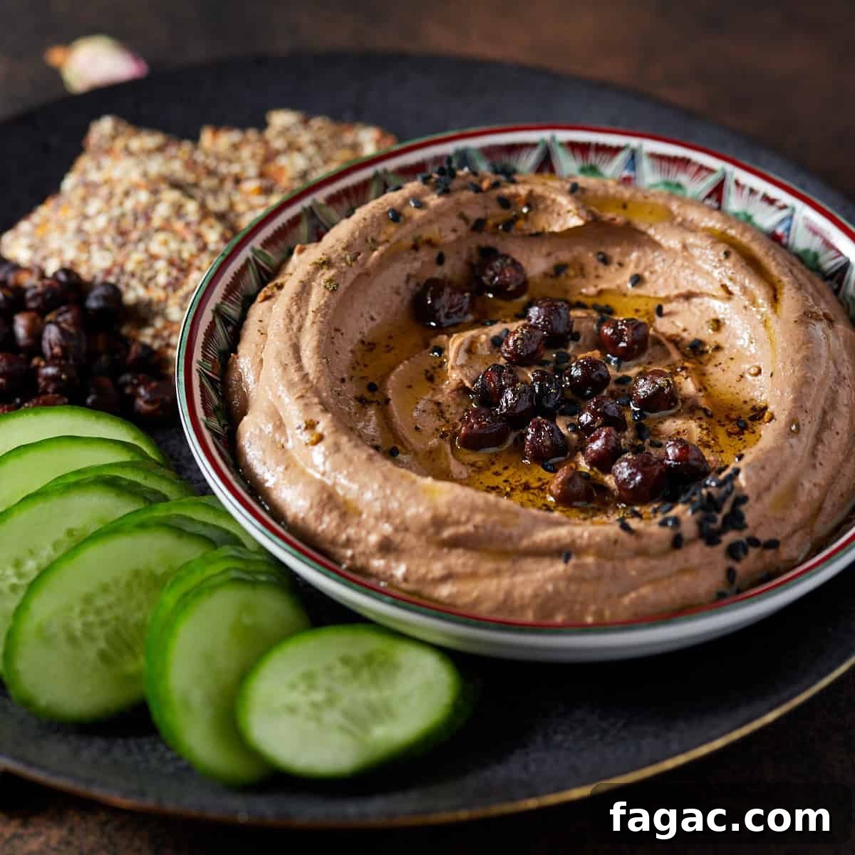 Image of black chickpea hummus garnished and set in a shallow patterned dish.