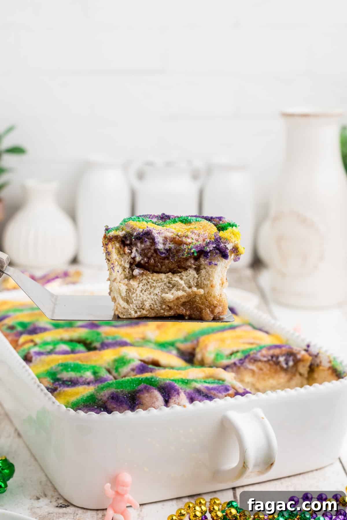 King Cake Cinnamon Roll Recipe: Sweet New Orleans Breakfast 5 A pan full of king cake cinnamon rolls with one being lifted out.