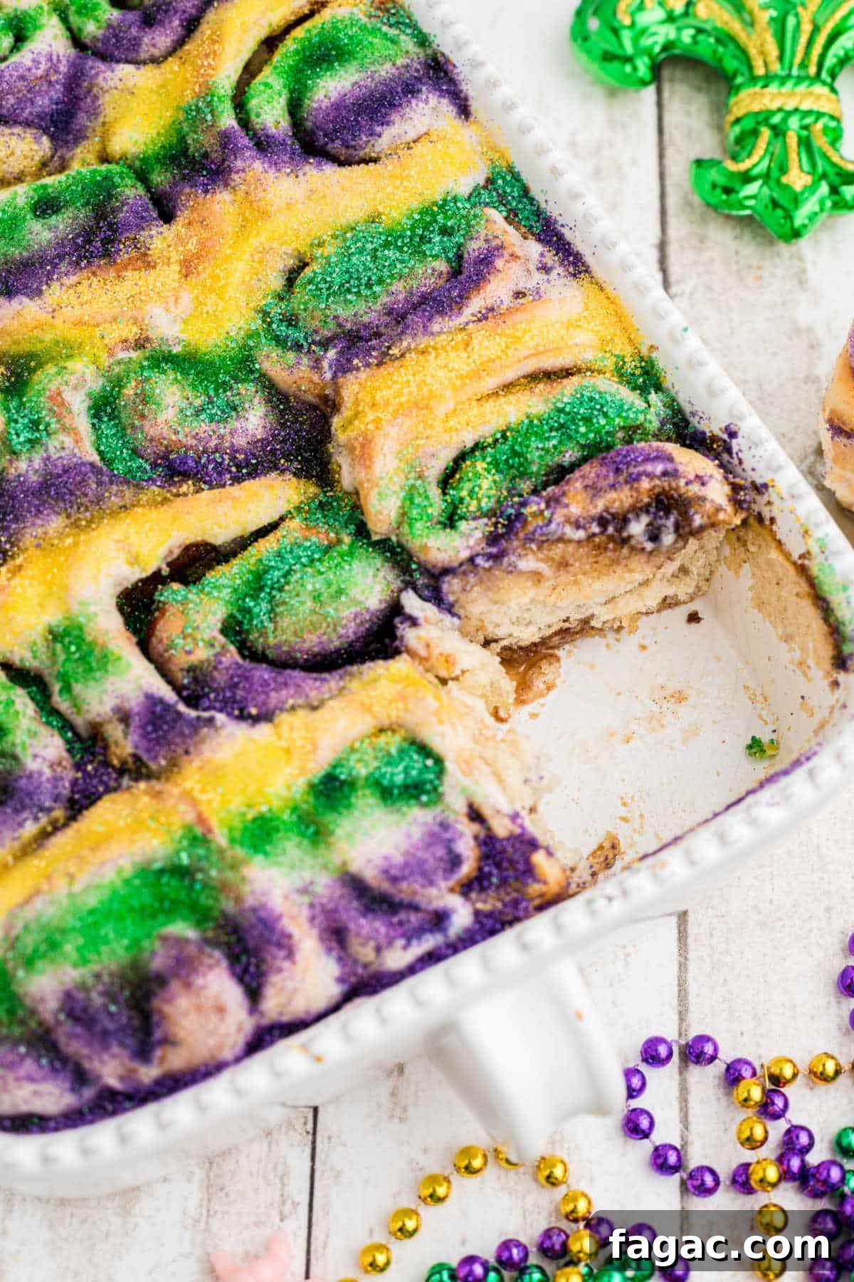 King Cake Cinnamon Roll Recipe: Sweet New Orleans Breakfast 6 Angled shot of a pan full of king cake cinnamon rolls with one taken.