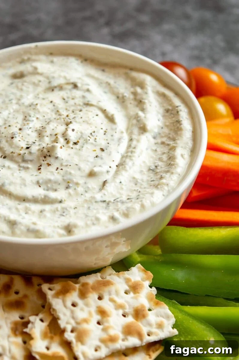 Creamy Herbed Cottage Cheese Dip — Boursin-Style Recipe 6 A white bowl of creamy dip with vegetable crudites in the background.