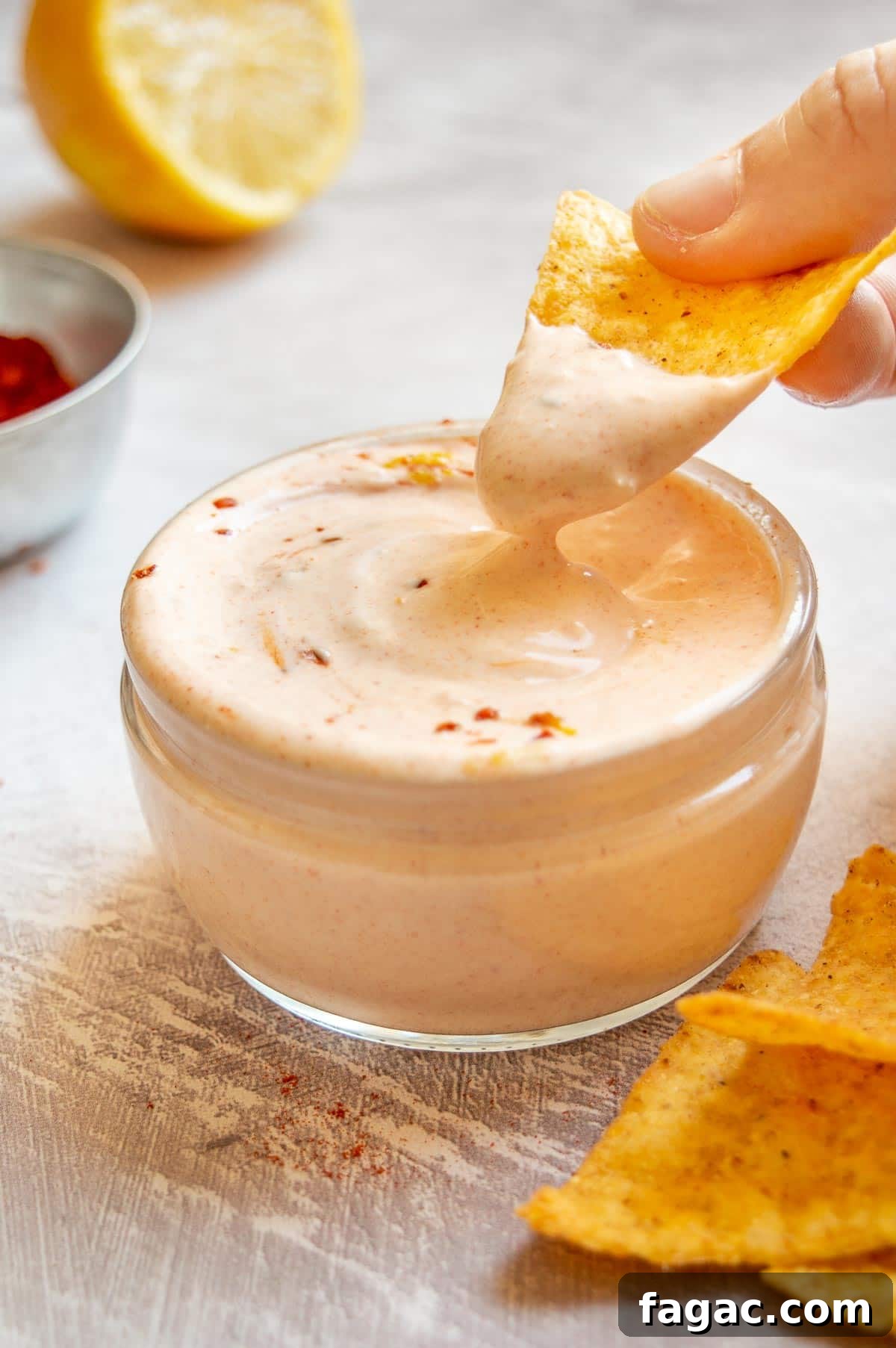 Creamy Herbed Cottage Cheese Dip — Boursin-Style Recipe 7 A hand dipping a yellow tortilla chip into a thick crema dip with a slight orange tinge.