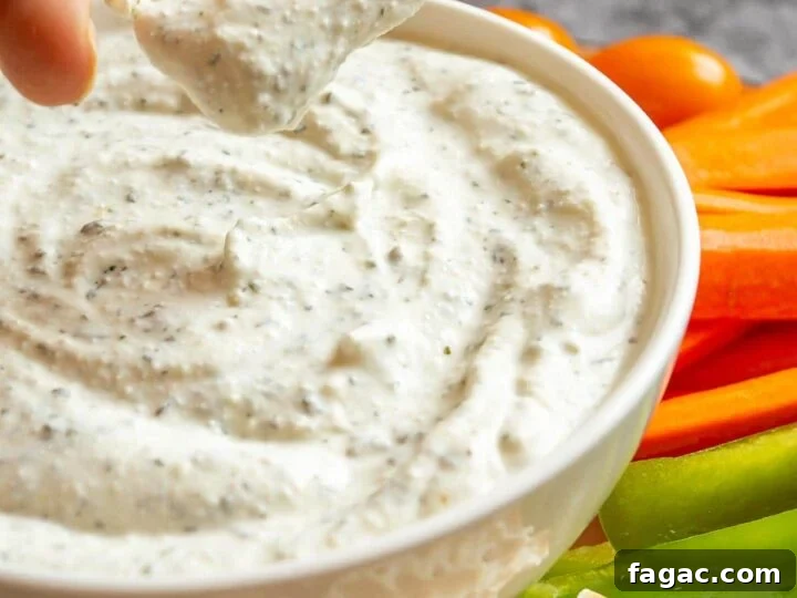 A hand dipping a cracker into a bowl of creamy pale herbed dip.