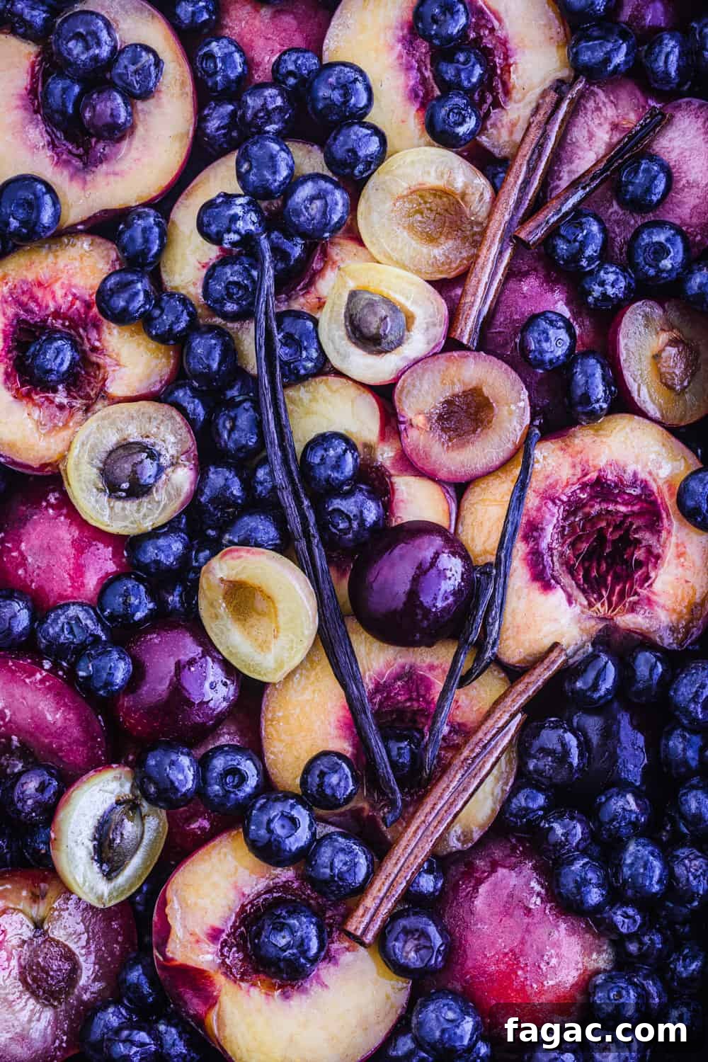 raw stone fruit and blueberries with vanilla beans and cinnamon sticks on a baking sheet being prepped to be cooked.