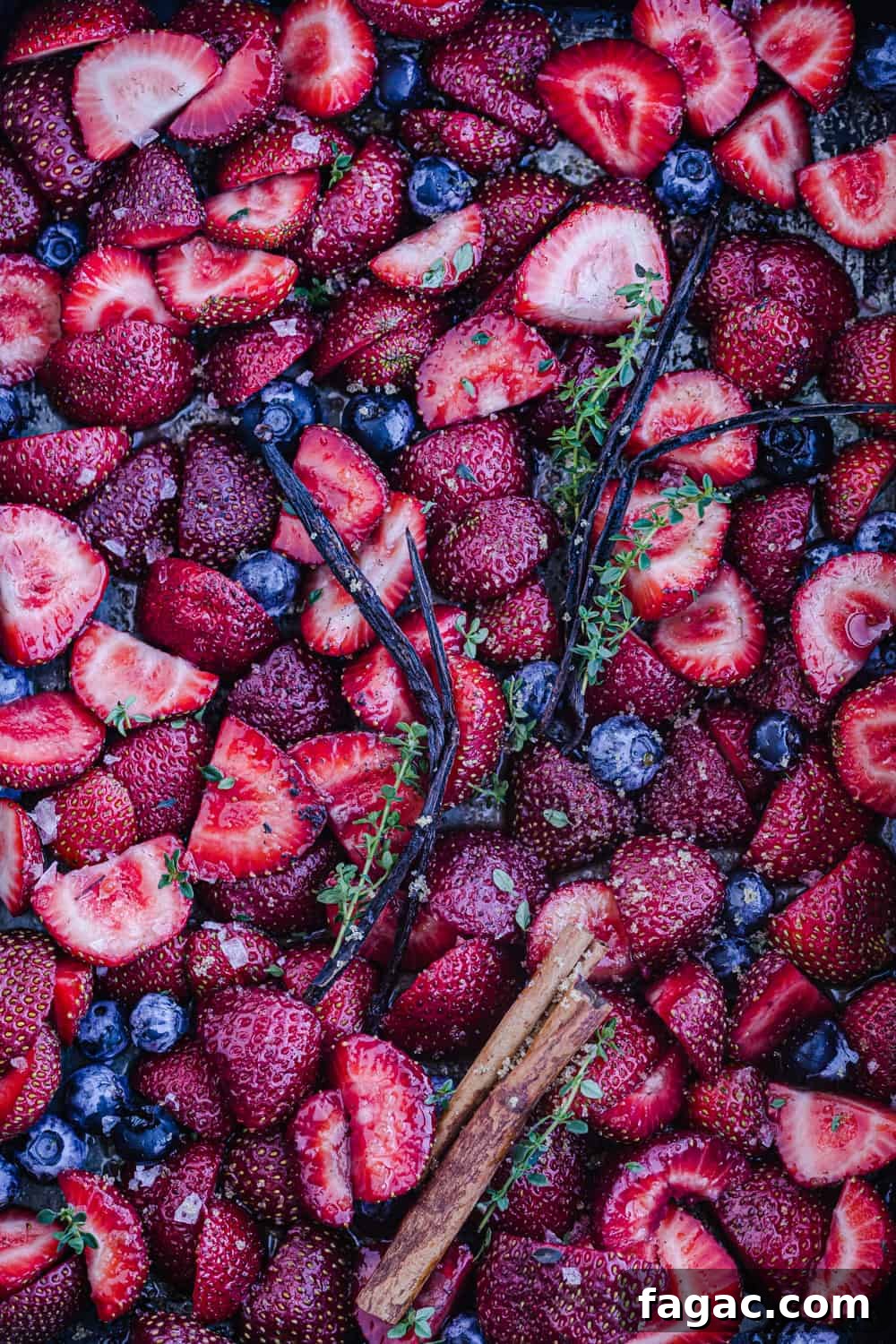 Raw strawberries and blueberries on a baking sheet being prepped to be cooked, overhead shot.