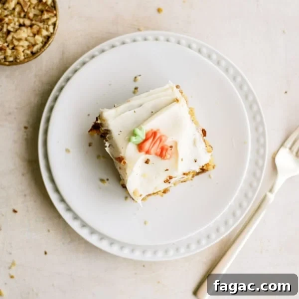 A slice of frosted cake with decorative icing sits on a white plate next to a fork; a small bowl of chopped nuts is nearby.