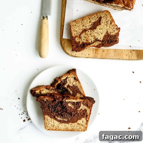 Two slices of a marbled loaf cake on a white plate, with more slices and a knife on a wooden cutting board nearby. Crumbs are scattered on the white surface.