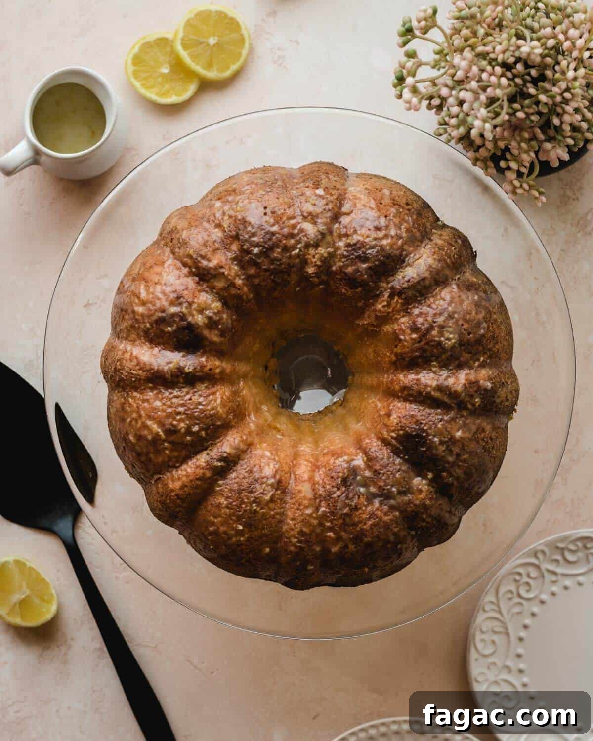 Authentic Italian Lemon Pound Cake Recipe with Zesty Glaze 4 Top view of an Italian lemon pound cake sitting on a cake plate with buttermilk lemon glaze in a carafe beside it alongside lemon rounds.