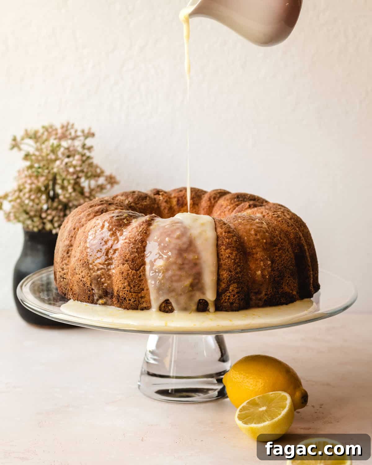 Authentic Italian Lemon Pound Cake Recipe with Zesty Glaze 6 Small carafe of buttermilk lemon glaze pouring over the top of an Italian lemon pound cake sitting on a cake display.