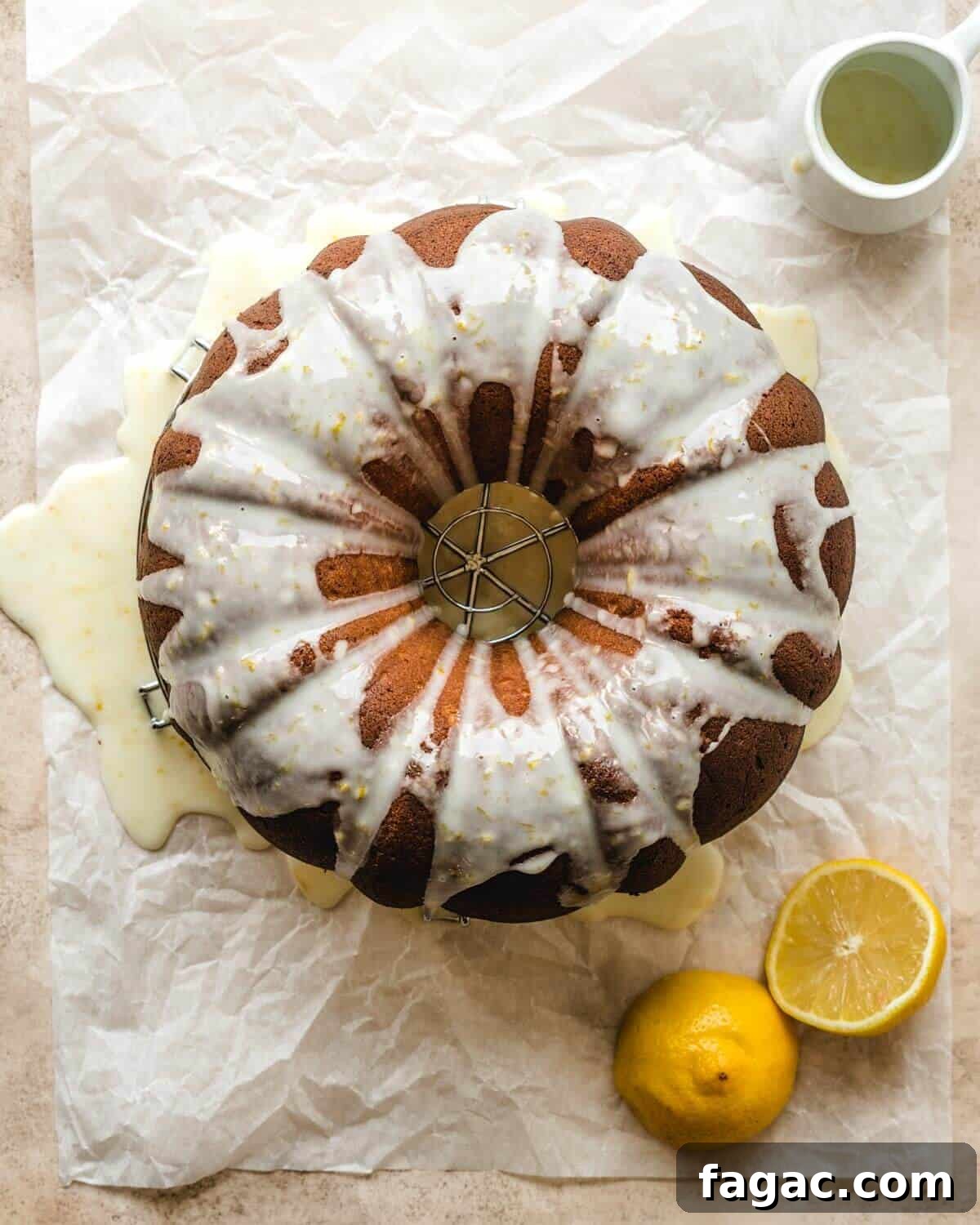 Authentic Italian Lemon Pound Cake Recipe with Zesty Glaze 7 Parchment paper with an Italian lemon pound cake sitting on a cooling rack, topped with glaze and lemons cut in half next to it.