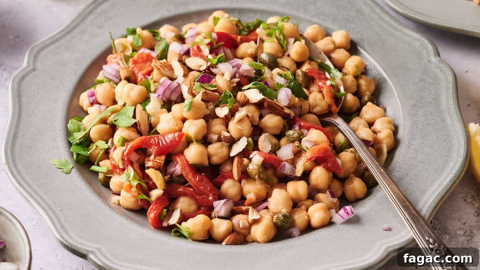 21 Easter Salad Ideas to Refresh Your Holiday Table 16 A plate of chickpea salad with chopped red onions, roasted red peppers, herbs, and sliced almonds, served with a spoon.