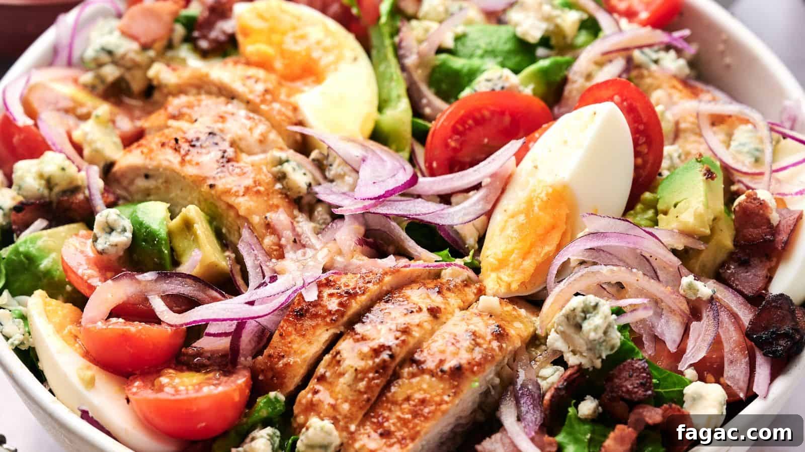 21 Easter Salad Ideas to Refresh Your Holiday Table 17 A close-up of a Cobb salad featuring sliced chicken, cherry tomatoes, avocado, boiled eggs, red onion, bacon bits, and blue cheese crumbles on a bed of lettuce.