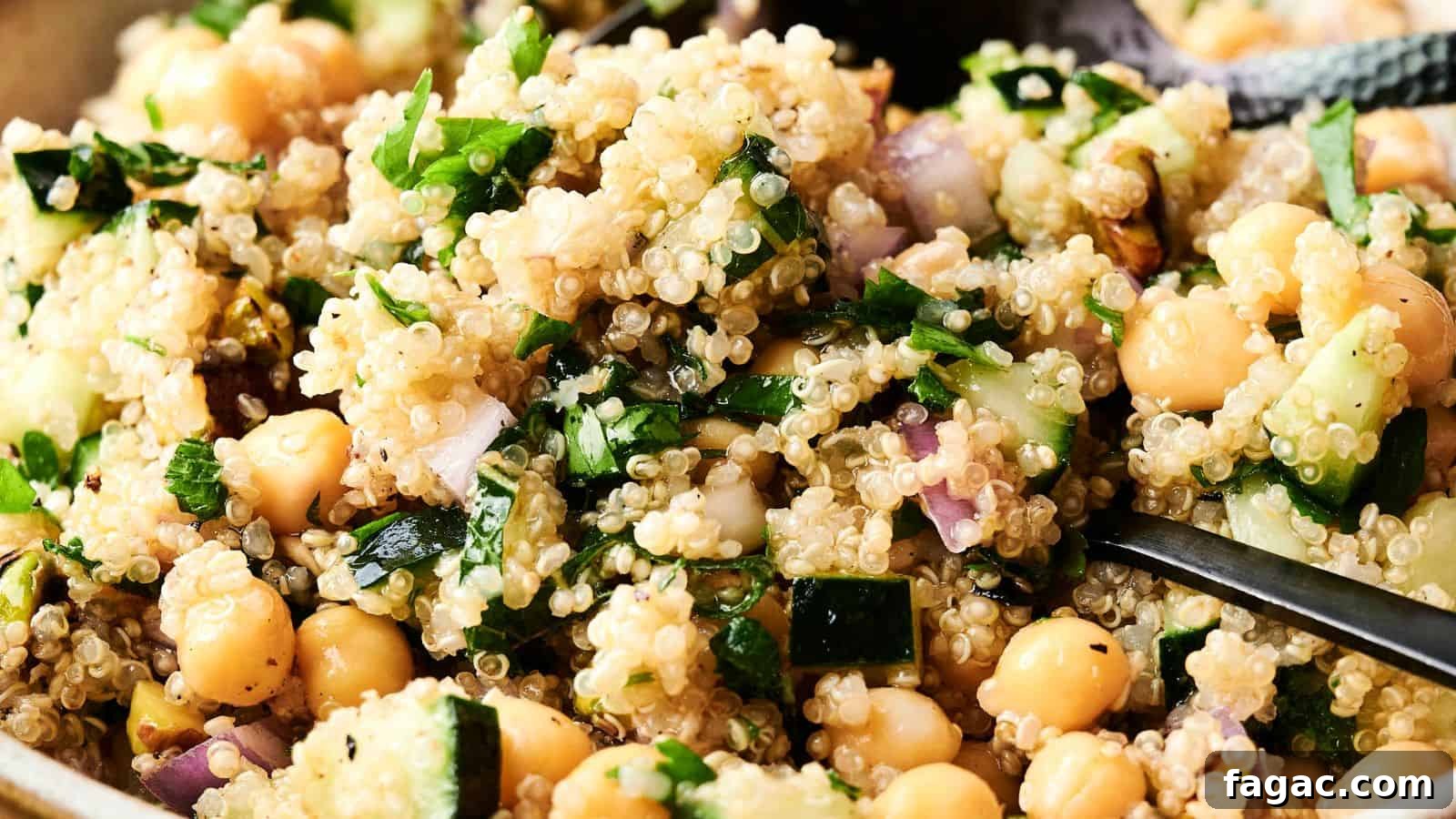 21 Easter Salad Ideas to Refresh Your Holiday Table 18 Close-up of a quinoa salad with chickpeas, chopped cucumber, parsley, red onion, and a light dressing, with a spoon partially visible.