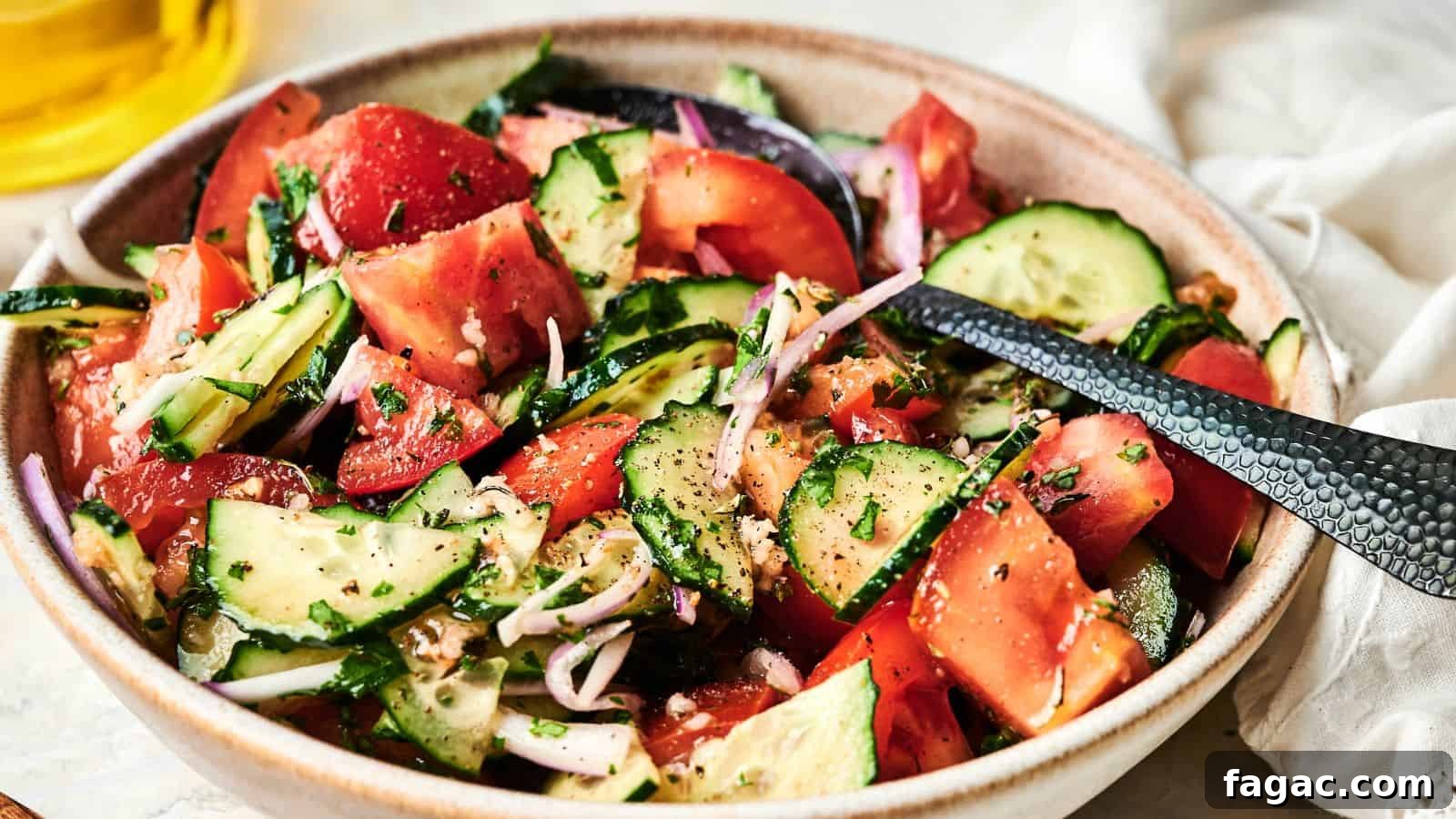21 Easter Salad Ideas to Refresh Your Holiday Table 4 A bowl of fresh salad with sliced tomatoes, cucumbers, red onions, and herbs, seasoned with black pepper, with a serving spoon.
