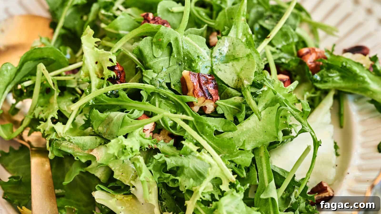 21 Easter Salad Ideas to Refresh Your Holiday Table 6 A close-up of a fresh green salad with mixed leafy greens, cucumber slices, and pecans on a plate with a gold fork.