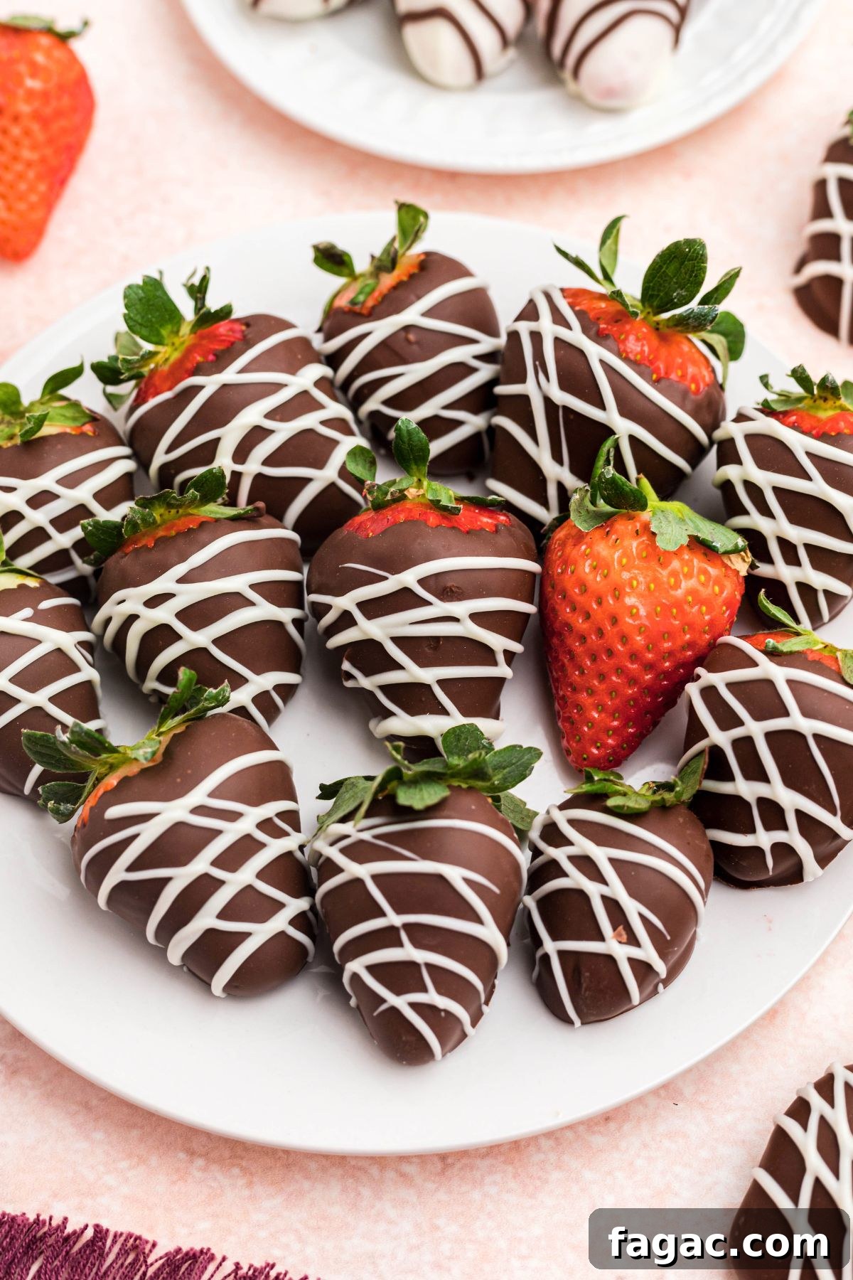 How to Make Chocolate-Covered Strawberries 2 Chocolate strawberries on a white plate sitting on a pink table.