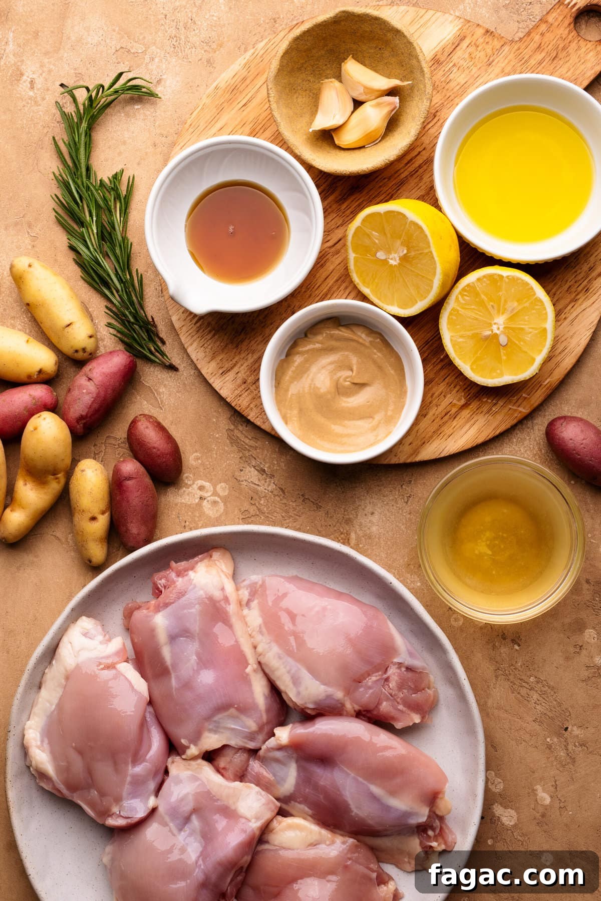Crispy Roasted Lemon & Rosemary Chicken Thighs with Potatoes 3 Ingredients for lemon rosemary chicken arranged in small bowls and a plate. The background is tan with a small round cutting board used as a background too.