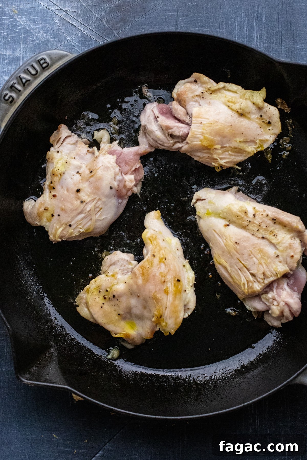Crispy Roasted Lemon & Rosemary Chicken Thighs with Potatoes 6 chicken thighs being browned in black skillet pan.