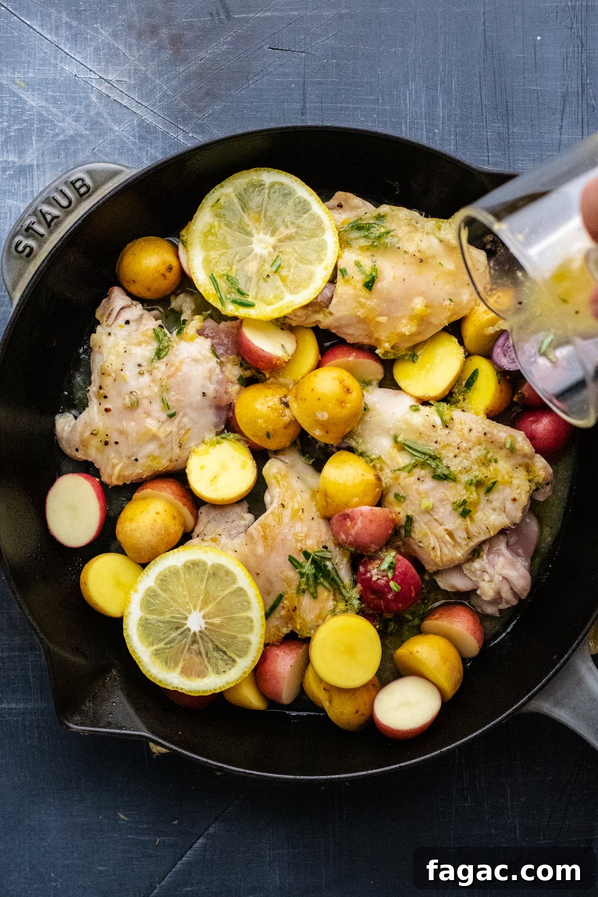 Crispy Roasted Lemon & Rosemary Chicken Thighs with Potatoes 7 glass jar pouring sauce over lemon rosemary chicken in black skillet pan.