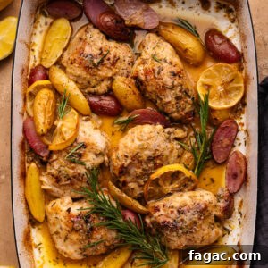 Crispy Roasted Lemon & Rosemary Chicken Thighs with Potatoes 10 Lemon rosemary chicken with potatoes in a rectangle-shaped roasting pan. The pan is displayed on a tan background with lemon slices and a dark gray napkin arranged around it.