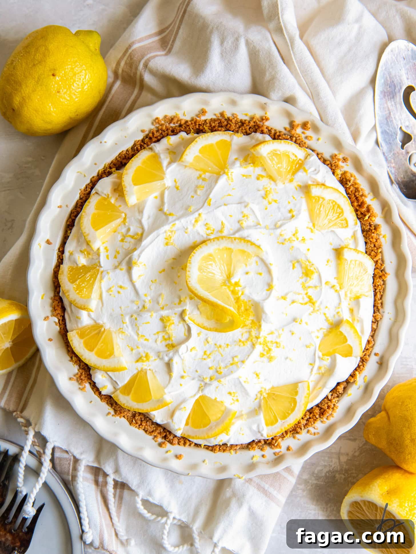 Creamy Lemon Icebox Pie Recipe 5 tabletop with uncut lemon icebox pie topped with whipped cream and lemon garnished.