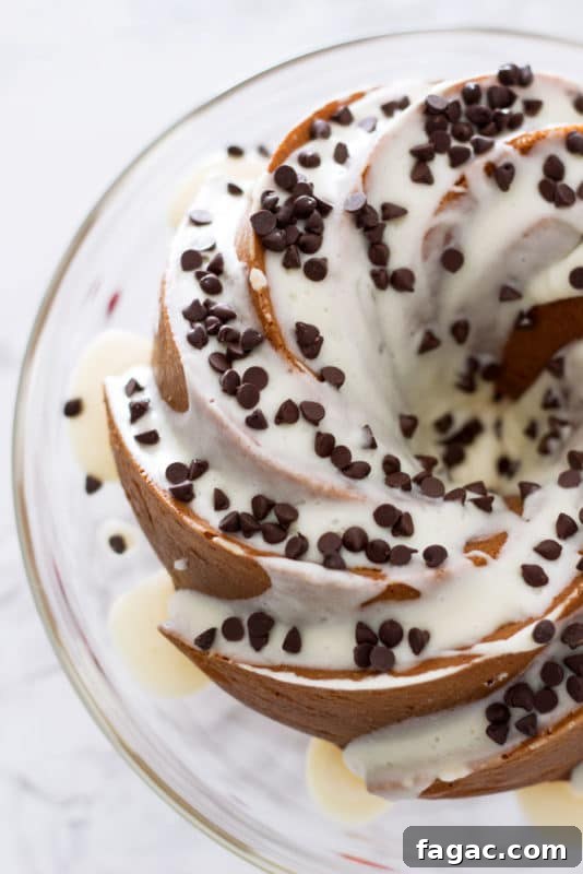 Orange Vanilla Bundt Cake topped with cream cheese frosting and mini chocolate chips, sitting on a glass cake dish.
