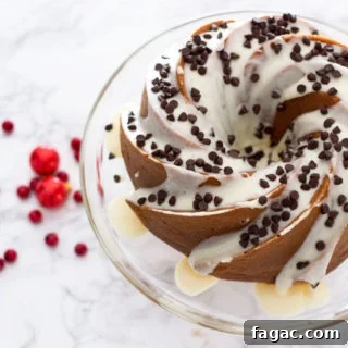 Glass cake dish containing an Orange Vanilla Bundt Cake topped with cream cheese frosting and mini chocolate chips sitting on a marble table.