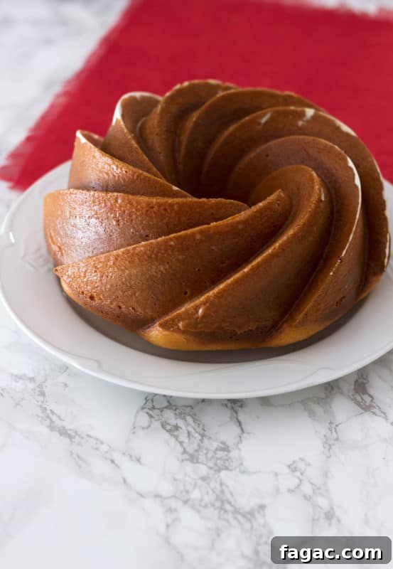 Side view of an Orange Vanilla Bundt Cake sitting on a white plate on a marble table, red tablecloth on table.