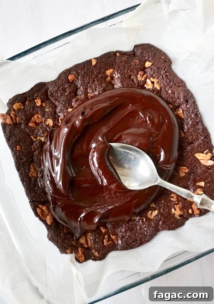 Fudgy Paleo Brownies with Rich Chocolate Frosting Recipe 3 coconut cream chocolate frosting being spooned on top of paleo chocolate brownie in a pyrex baking dish