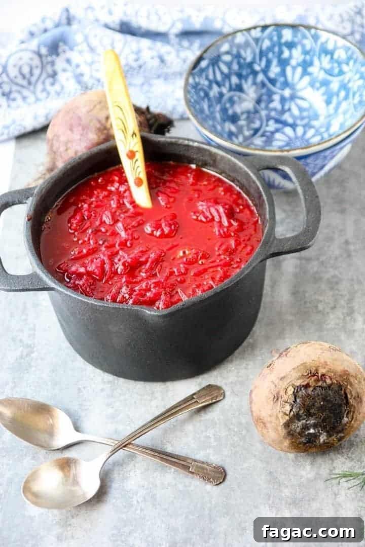 Authentic Ukrainian Borscht Recipe: Beet Soup 3 red beet soup in black pot with wooden spoon next to blue and white floral bowl and two silver spoons