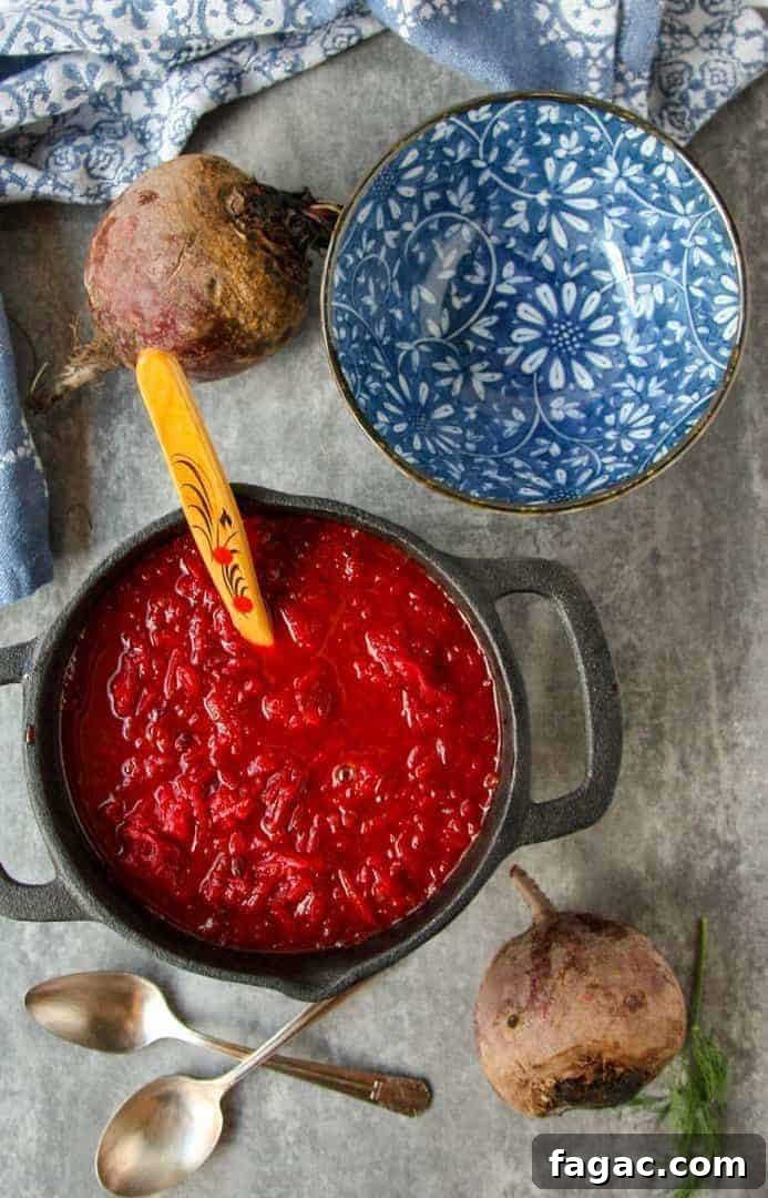 Authentic Ukrainian Borscht Recipe: Beet Soup 4 top shot of red beet soup in black pot with wooden spoon next to blue and white floral bowl and two silver spoons