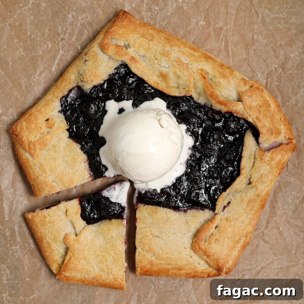 Rustic Blueberry Galette with Buttery Flaky Crust 3 A rustic Blueberry Galette with a golden, folded crust sits on brown parchment paper, cut into three pieces and topped with a scoop of vanilla ice cream.