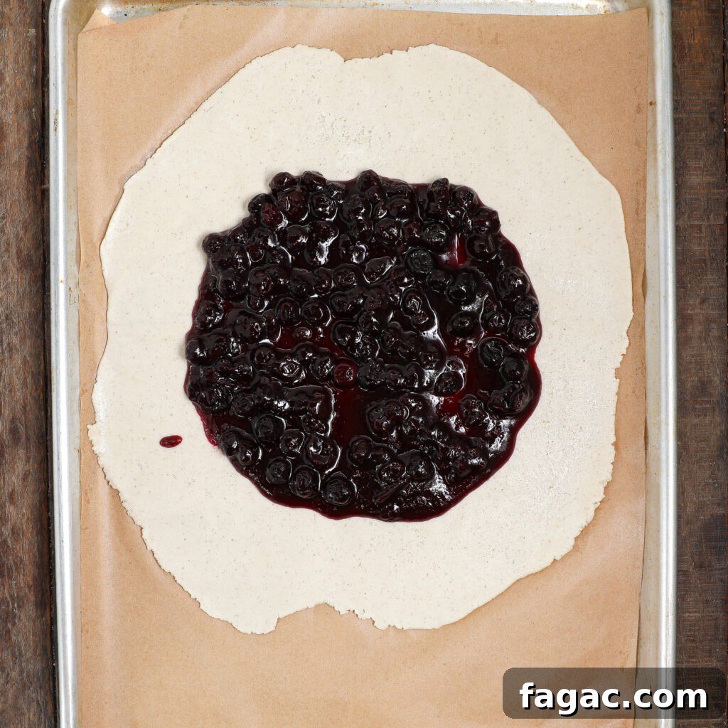 Rustic Blueberry Galette with Buttery Flaky Crust 4 A sheet of dough rolled out on parchment paper with blueberry filling spread in the center, ready to be folded into a rustic Blueberry Galette and baked on a metal tray.