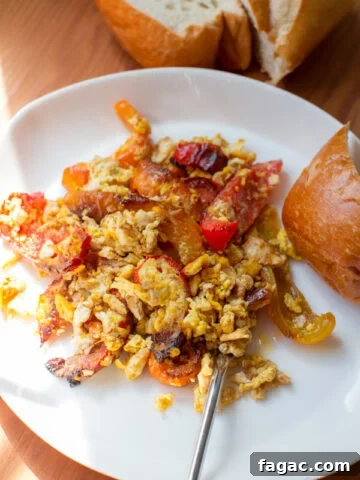 scrambled eggs and seared bell peppers with a side of bread on a plate