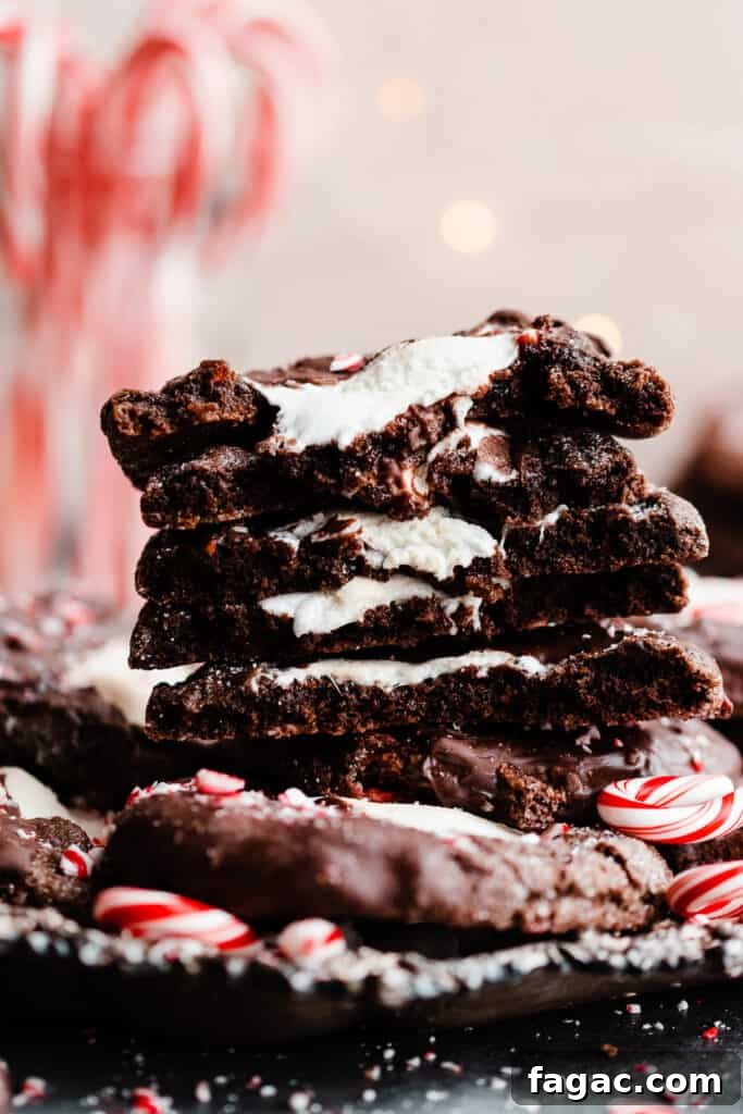 Gooey Peppermint Hot Chocolate Cookies with Marshmallows 2 A close up of a stack of the broken open hot chocolate cookies with twinkle lights and candy canes in the background.
