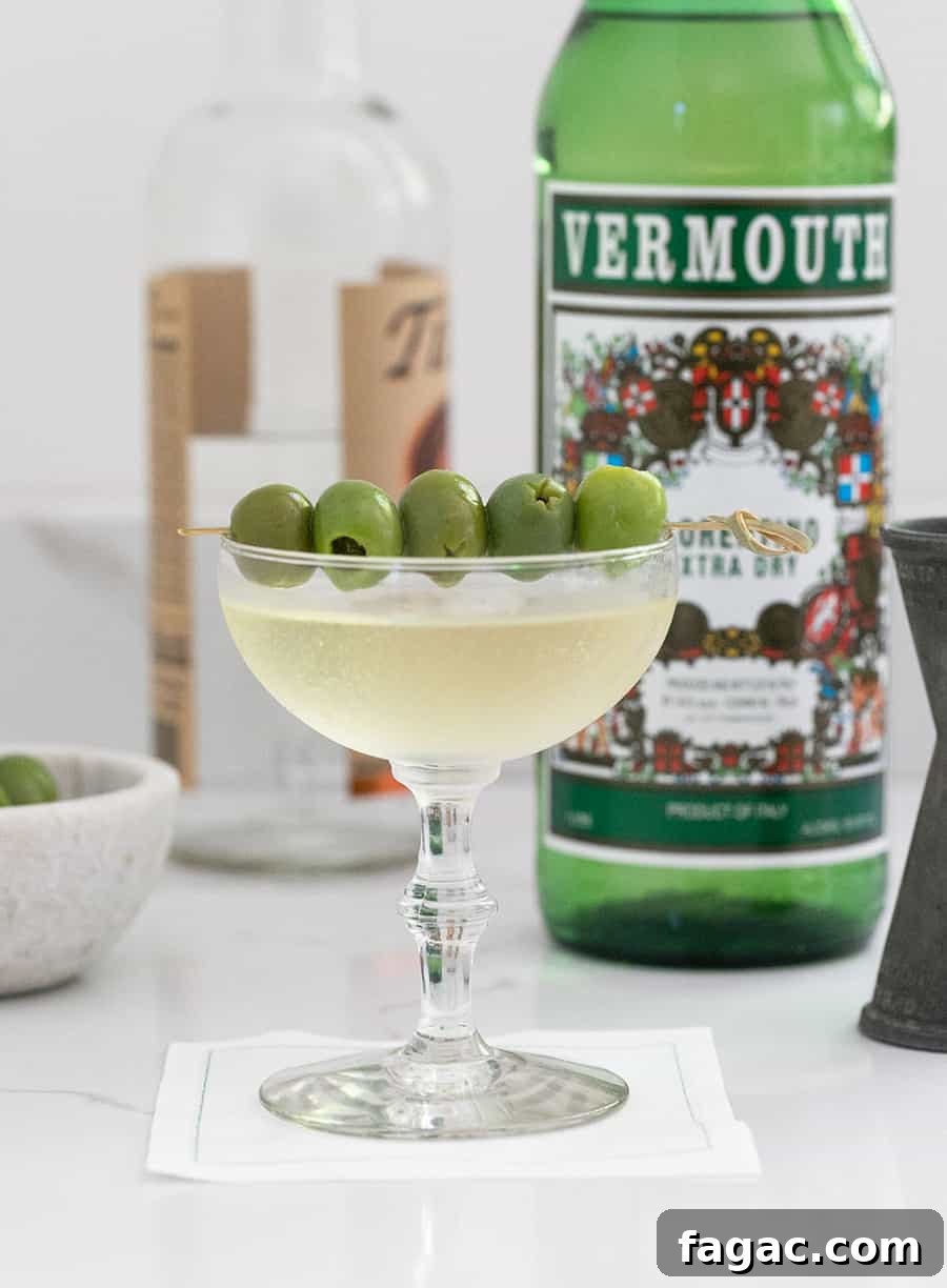 Dirty Martini Recipe: Tips for the Classic Cocktail 3 Dirty martini in a coupe with olives and a bottle of Vermouth in the back.