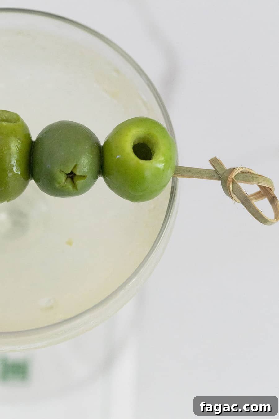 Dirty Martini Recipe: Tips for the Classic Cocktail 6 Green olives on a pick laying over a dirty martini.
