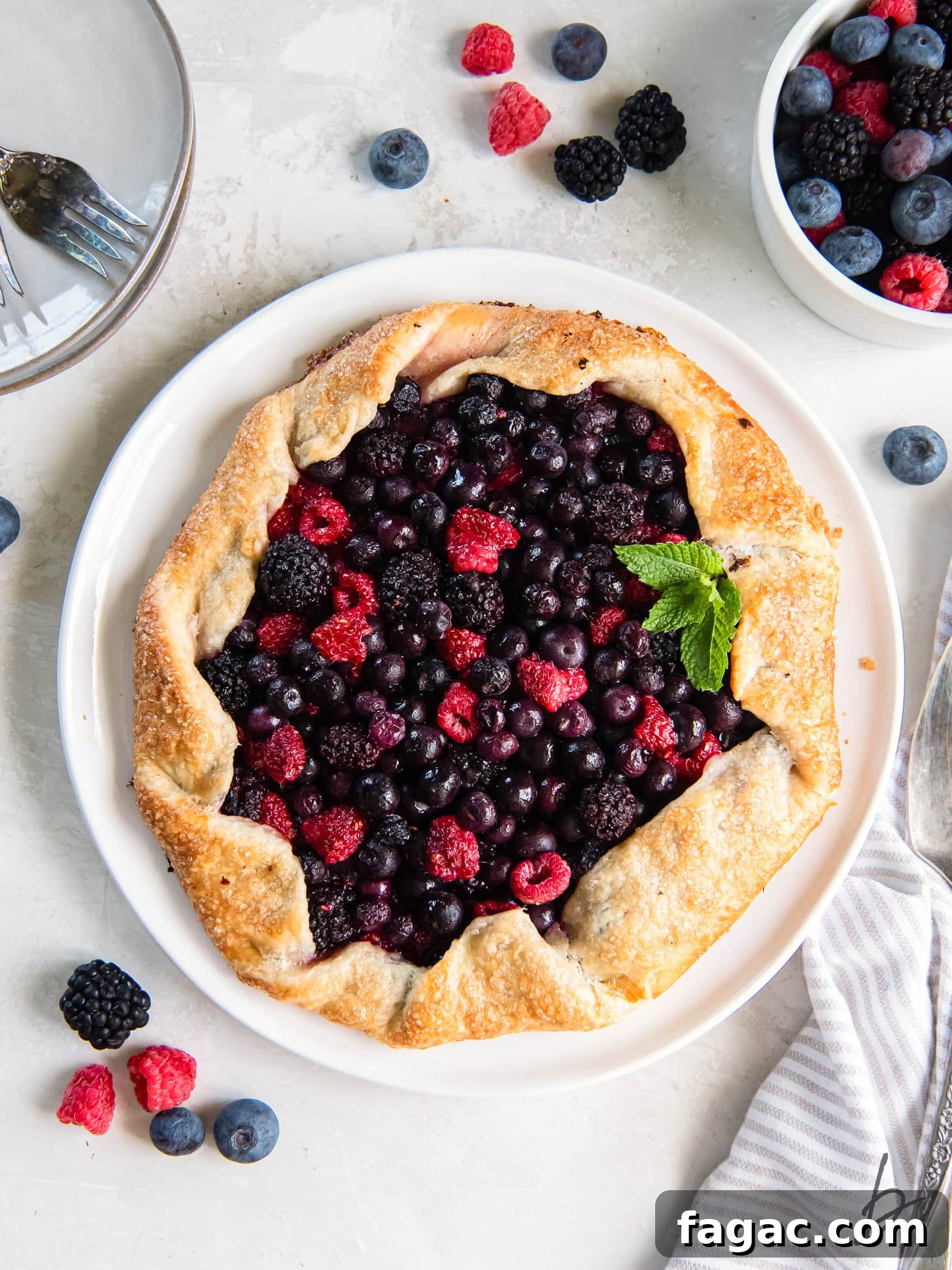Summer Mixed Berry Galette with Flaky Crust 7 mixed berry galette on a white plate on a tabletop with some fresh berries.