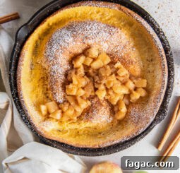 apple dutch baby in a skillet with hand wrapped with kitchen towel.
