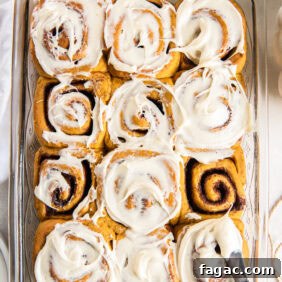 Pumpkin Spice Cinnamon Rolls with Maple Glaze 12 13x9 baking dish with pumpkin spice cinnamon rolls being frosted with cream cheese icing.