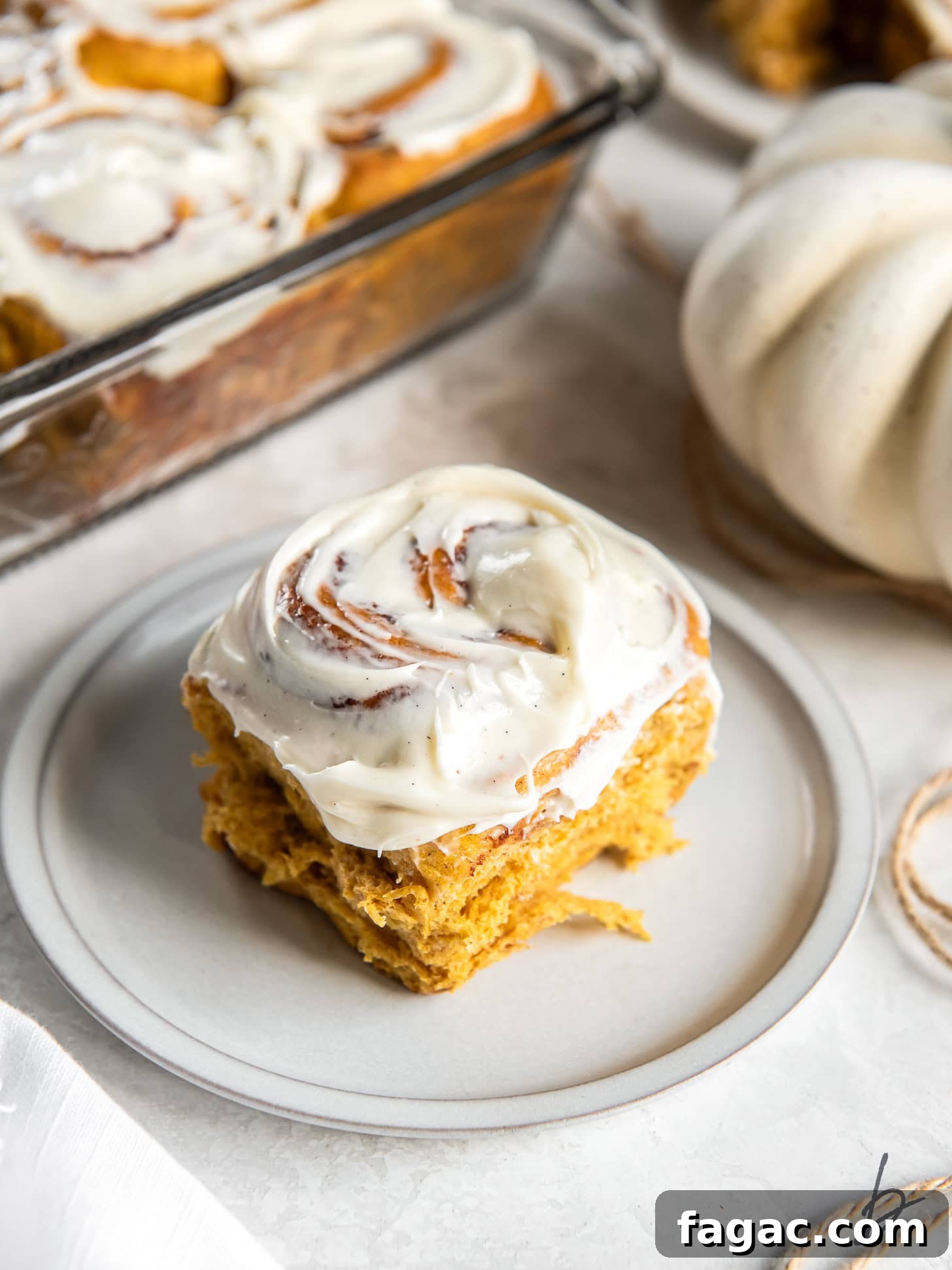 Pumpkin Spice Cinnamon Rolls with Maple Glaze 7 pumpkin cinnamon roll with cream cheese icing on a small round plate on a tabletop.