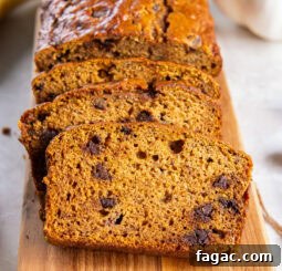 pumpkin banana bread sliced with chocolate chips leaning against loaf on cutting board.